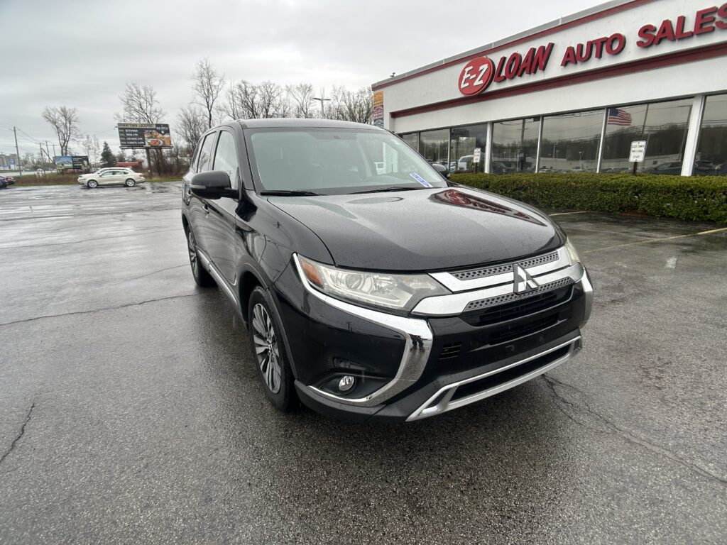 Black SUV parked in a wet lot in front of an EZ Loan Auto Sales storefront on a cloudy rainy day.