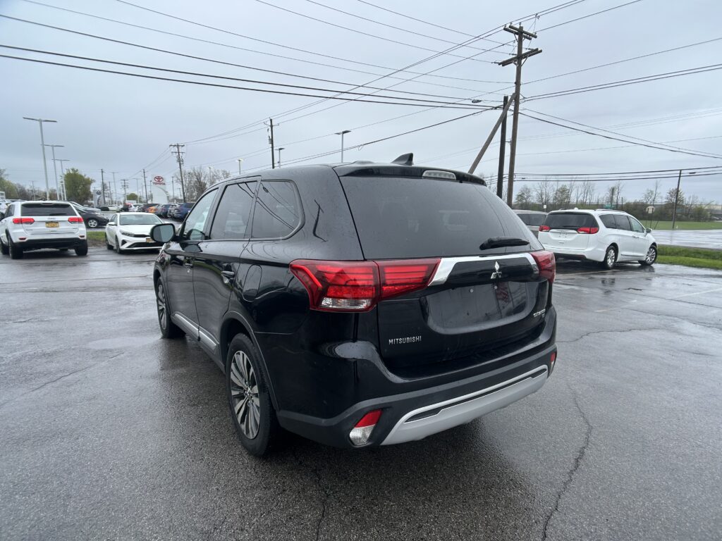 Rear view of a black Mitsubishi SUV in a wet parking lot at a car dealership, with other cars and overhead power lines in the scene.