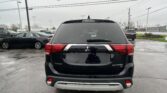 Rear view of a black Mitsubishi Outlander SE in a parking lot on a rainy day, with other cars and overhead power lines in the background.