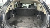 Open rear hatch of an SUV showing the cargo area with third-row seats upright and a textured black rubber mat behind them.