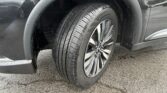 Close-up of a car's front wheel and fender showing a wet tire with an alloy rim and mud splatters on the wheel well and surrounding body.