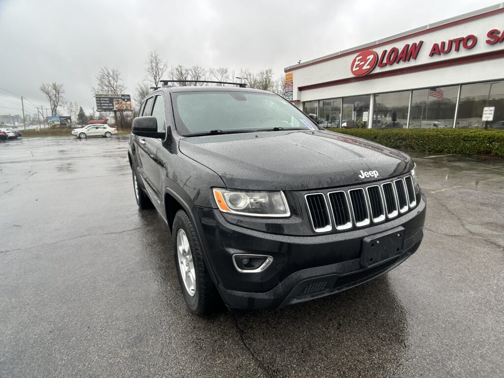 Black Jeep SUV parked in a wet lot in front of an E-Z Loan Auto dealership sign railing the background with rain droplets on the vehicle surface.