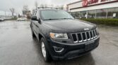 Black Jeep SUV parked in a wet lot in front of an E-Z Loan Auto dealership sign railing the background with rain droplets on the vehicle surface.