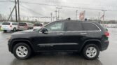 Black Grand Cherokee SUV in foreground at a car dealership lot on a wet day, with a service sign and power lines in the background
