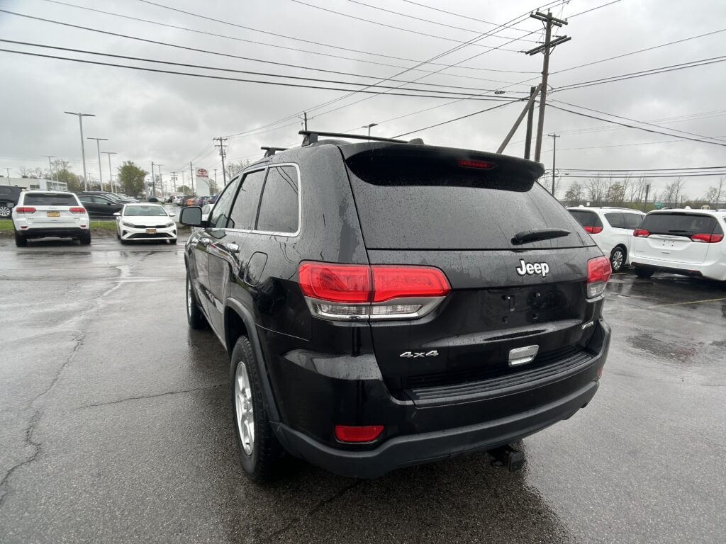 Black Jeep SUV (4x4) photographed from the rear in a rainy dealership lot with other cars and power lines overhead.