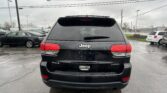 Rear view of a black Jeep Grand Cherokee Laredo 4x4 in a wet parking lot on a cloudy day with raindrops on the window surface.