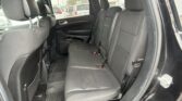 Black fabric rear passenger seating of an SUV with three seats, visible headrests, and buckled seat belts; rainy window view outside.”,