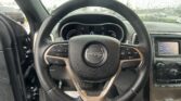 Close-up of a Jeep steering wheel inside a car, with a rain-splattered windshield and dashboard in the background