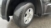 Close-up of a car tire mounted on a silver wheel inside the wheel well of a dark vehicle.
