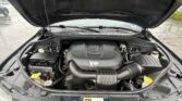 Open car hood revealing a V6 engine and surrounding engine bay components in a rainy parking lot