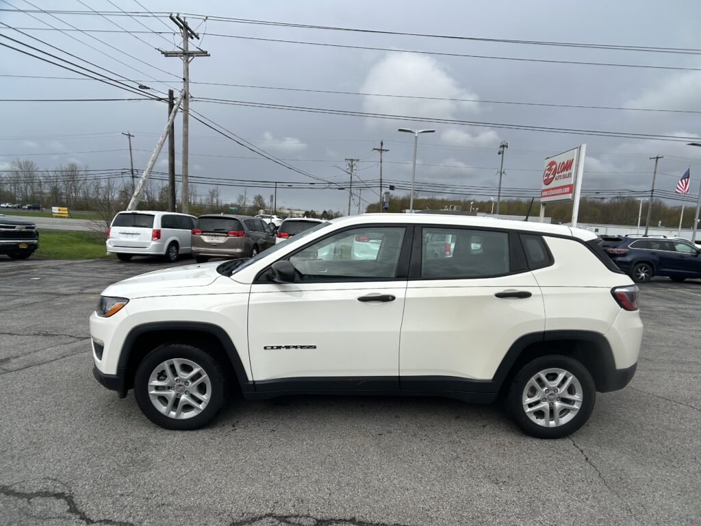 White Jeep Compass SUV in a car dealership lot with a large EZ Loan Auto Sales sign and an American flag in the background.