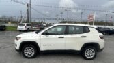 White Jeep Compass SUV in a car dealership lot with a large EZ Loan Auto Sales sign and an American flag in the background.