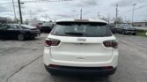 Rear view of a white Jeep SUV parked in a busy car lot, with other vehicles and power lines overhead under a cloudy sky.
