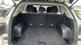 Open SUV cargo area with the third-row seats upright and black carpeting, view of the rear interior through the open hatch.