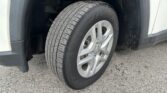 Close-up of a car tire on a silver alloy wheel, with the wheel well and dirt-splattered fender in view.