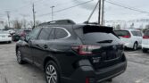 Black Subaru SUV in a parking lot with other cars and tall power lines overhead under a cloudy sky