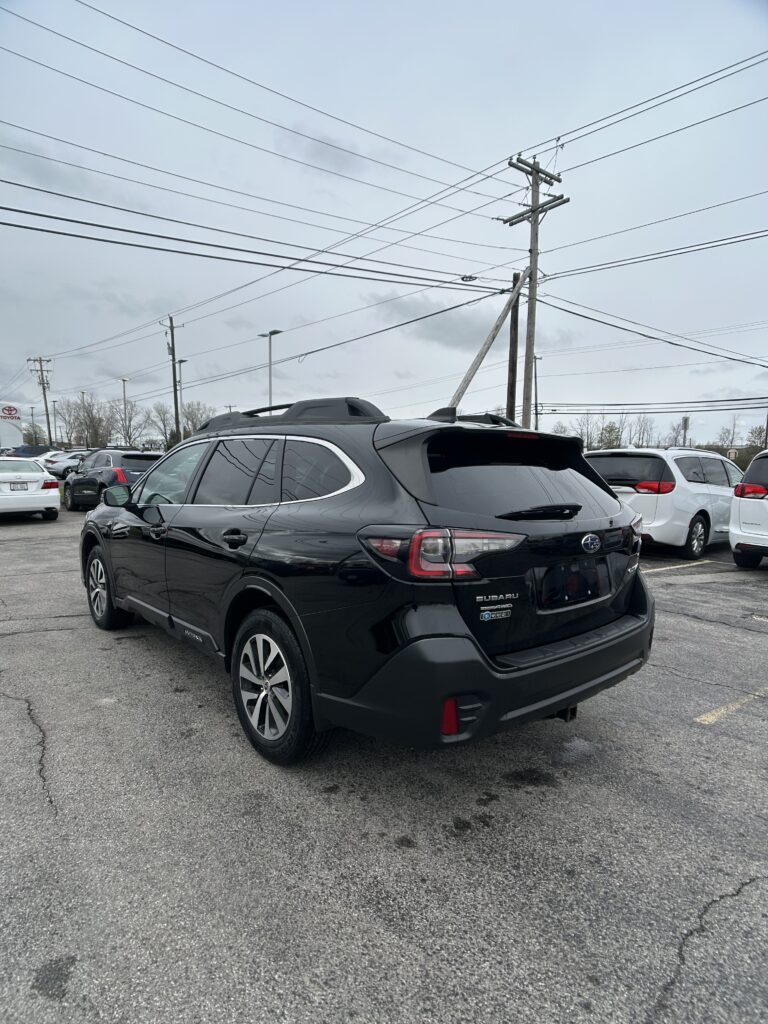 Black Subaru SUV in a parking lot with other cars and tall power lines overhead under a cloudy sky