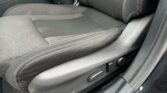 Front passenger seat area of a dark cloth car interior showing the center armrest, seatbelt buckle, and lower door sill with scuffed plastic wear on the edge.