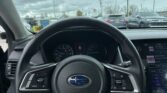 Driver's view from the driver's seat showing the steering wheel, instrument cluster, and a rain-speckled windshield with a parking lot outside.