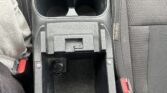 Center console between front seats with two cup holders and a small storage pocket beneath. Red seat belt buckles visible at sides.