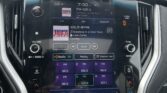 Car infotainment screen displaying FM radio (106.5 WYRK) with song info, time 7:30 PM, outside temp 55°F, surrounded by climate and control buttons; raindotted windshield visible outside the dashboard.