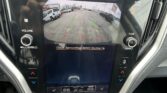 Infotainment screen showing rear‑view camera with colored guide lines for backing up and the message “Check Surroundings Before Backing Up.”