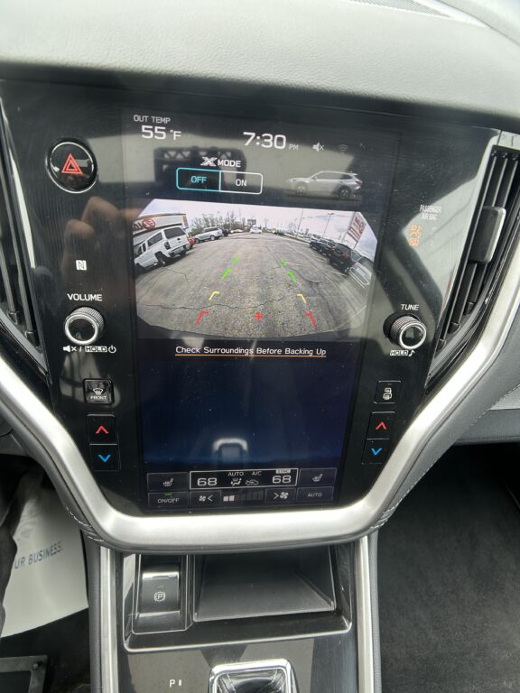 Infotainment screen showing rear‑view camera with colored guide lines for backing up and the message “Check Surroundings Before Backing Up.”