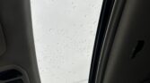 Interior of a car looking up at a sunroof with raindrops on the glass.
