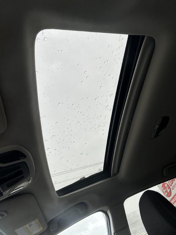 Interior of a car looking up at a sunroof with raindrops on the glass.