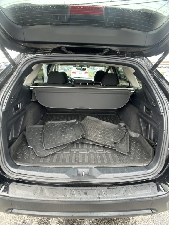 Open SUV trunk with multiple rubber cargo mats piled on the floor and a retractable cargo cover; rear seats are visible in the background.
