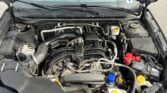 Open car hood showing engine bay with various hoses, wires, and reservoir caps visible under gray hood insulator