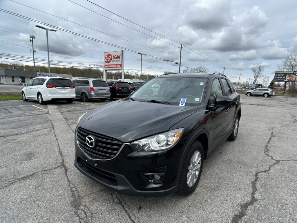 Black Mazda SUV in a car lot with other vehicles and a red-and-white EZ Loan Auto Sales sign in the background, cloudy sky above.