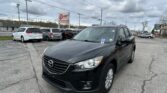 Black Mazda SUV in a car lot with other vehicles and a red-and-white EZ Loan Auto Sales sign in the background, cloudy sky above.