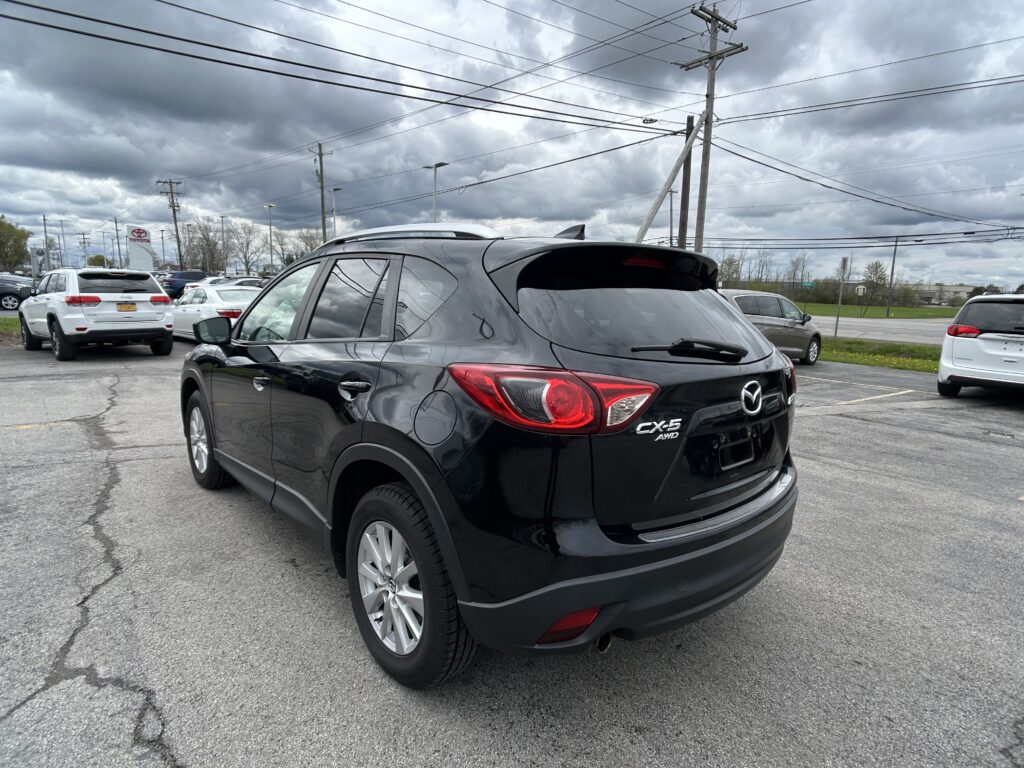 Close-up of a black Mazda CX-5 AWD parked in a car lot with other vehicles and an overcast sky.