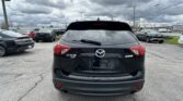 Rear view of a black Mazda CX-5 AWD in a busy parking lot under a cloudy sky, with other vehicles around.