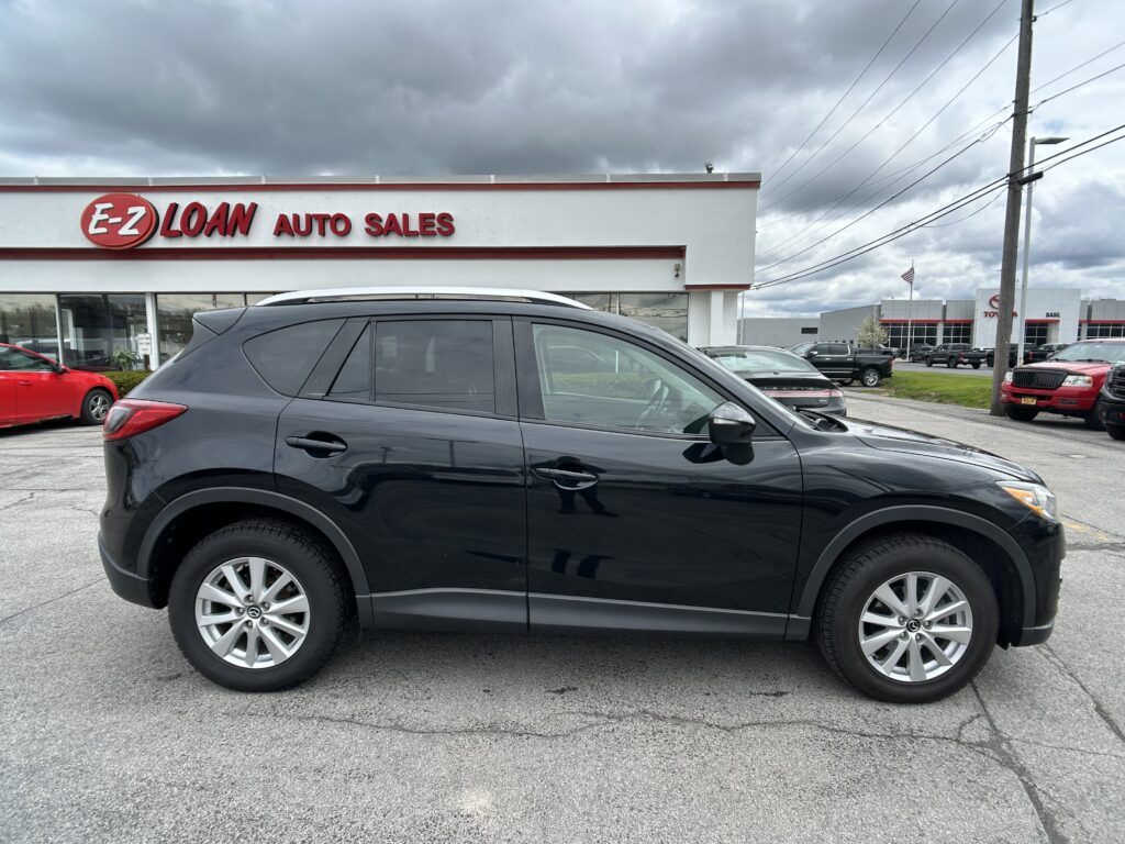 Front view of an auto dealership with the 'E‑Z LOAN AUTO SALES' sign; a dark SUV is in the foreground and other cars are in the lot under cloudy skies.