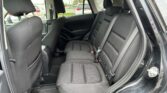 Back seats of a car with black fabric upholstery, three headrests and visible seat belts, seen through an open rear door.