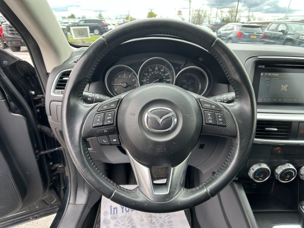 Driver's view of the black leather steering wheel and dashboard, with a parking lot visible through the windshield