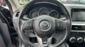 Driver's view of the black leather steering wheel and dashboard, with a parking lot visible through the windshield