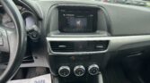 Interior of a car from the driver's seat with the center infotainment screen showing FM radio, climate controls below, and a flyer on the passenger side that reads 'We Take Pride In Your Vehicle!' in a dealership parking lot.