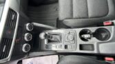 Interior of a car showing the center console with gear shifter, climate controls, two cup holders, and textured front seats; floor mat on the passenger side visible.