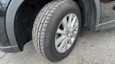 Close-up of a car’s front wheel and tire, showing the tread and silver alloy rim with a dark vehicle body and wheel well nearby on a paved surface.