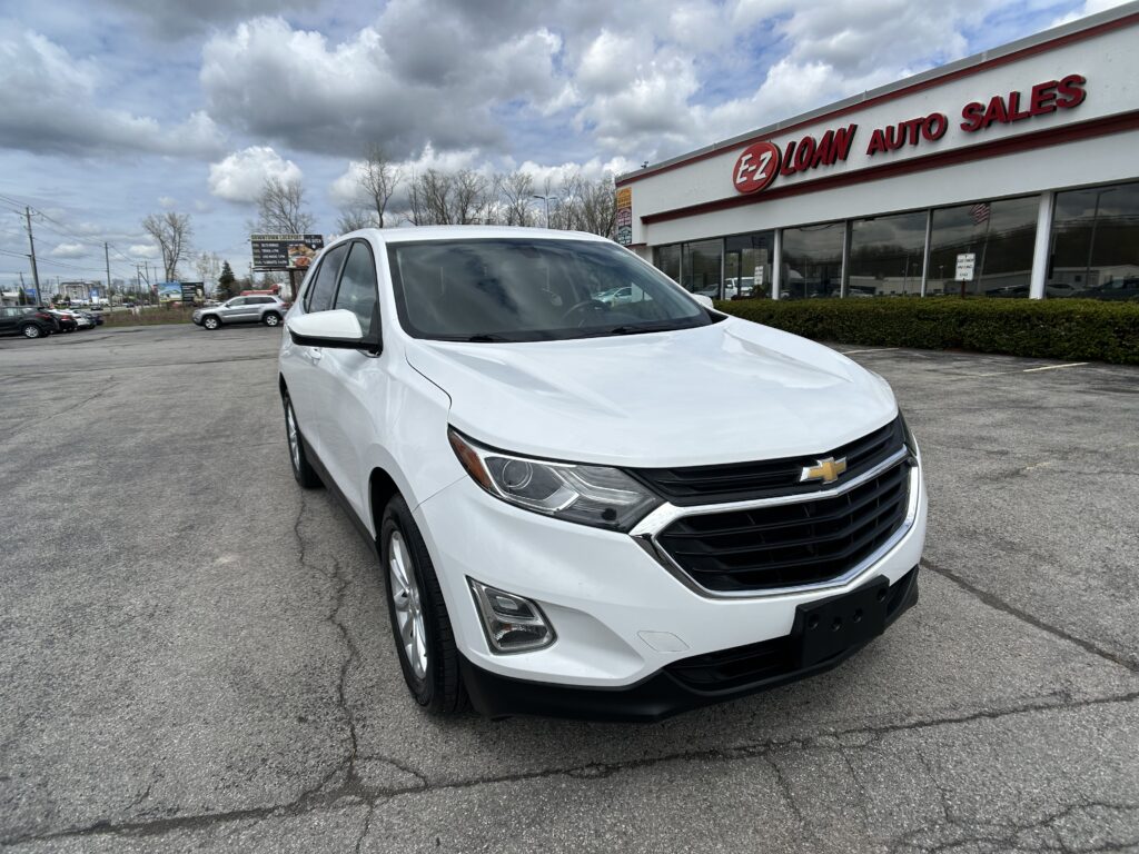White Chevrolet SUV parked in a dealership lot in front of an E-Z Loan Auto Sales storefront.