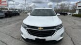 Front view of a white Chevrolet SUV at a car dealership lot, with other vehicles and a cloudy sky behind.