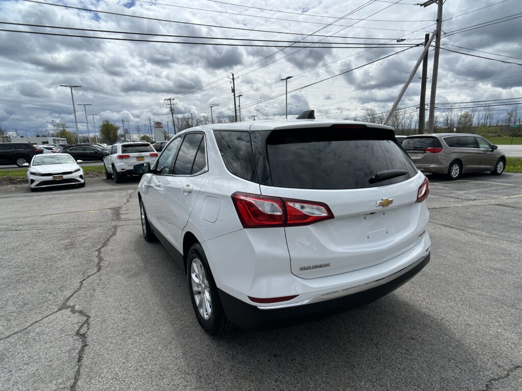 White Chevrolet SUV parked in a car lot with other vehicles and cloudy sky above.