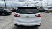Rear view of a white Chevrolet SUV in a busy parking lot with other cars and a cloudy sky overhead.