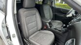 Front seat area of a car interior with black quilted seats and orange stitching, driver door open revealing door frame and weather seal.