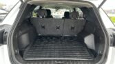 Open SUV trunk with three-row seating upright and a ribbed black cargo mat visible in the cargo area on the floor.