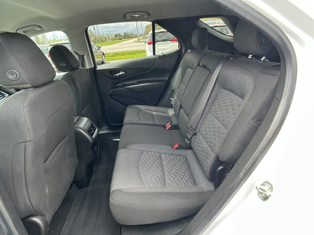 Interior view of a car's rear passenger area with black quilted seats, orange stitching, and three seat belts visible across the back row.