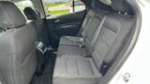 Interior view of a car's rear passenger area with black quilted seats, orange stitching, and three seat belts visible across the back row.